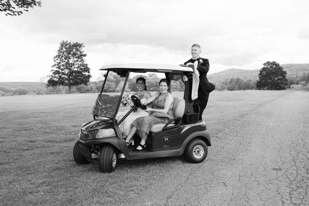 groom on back of golf cart while bride sits in passenger seat