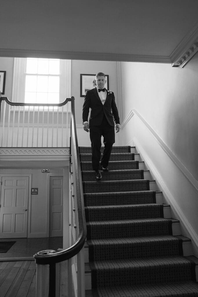 groom walking down the stairs in black and white photo