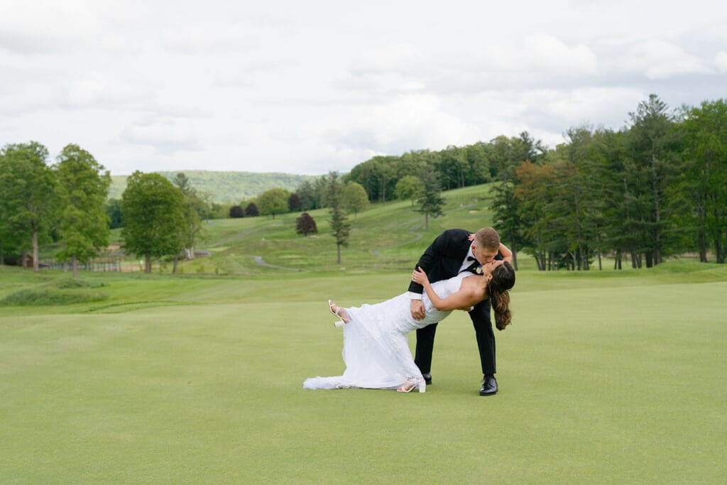 groom dips and kisses bride on a sprawling green golf course