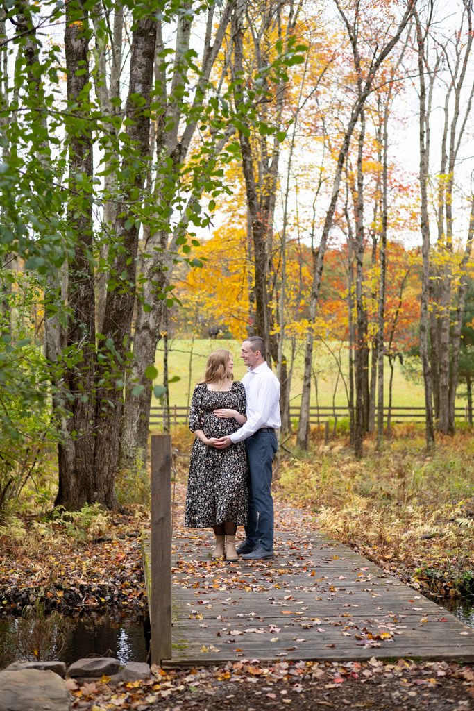 couple posing for maternity photos surrounded by fall foliage