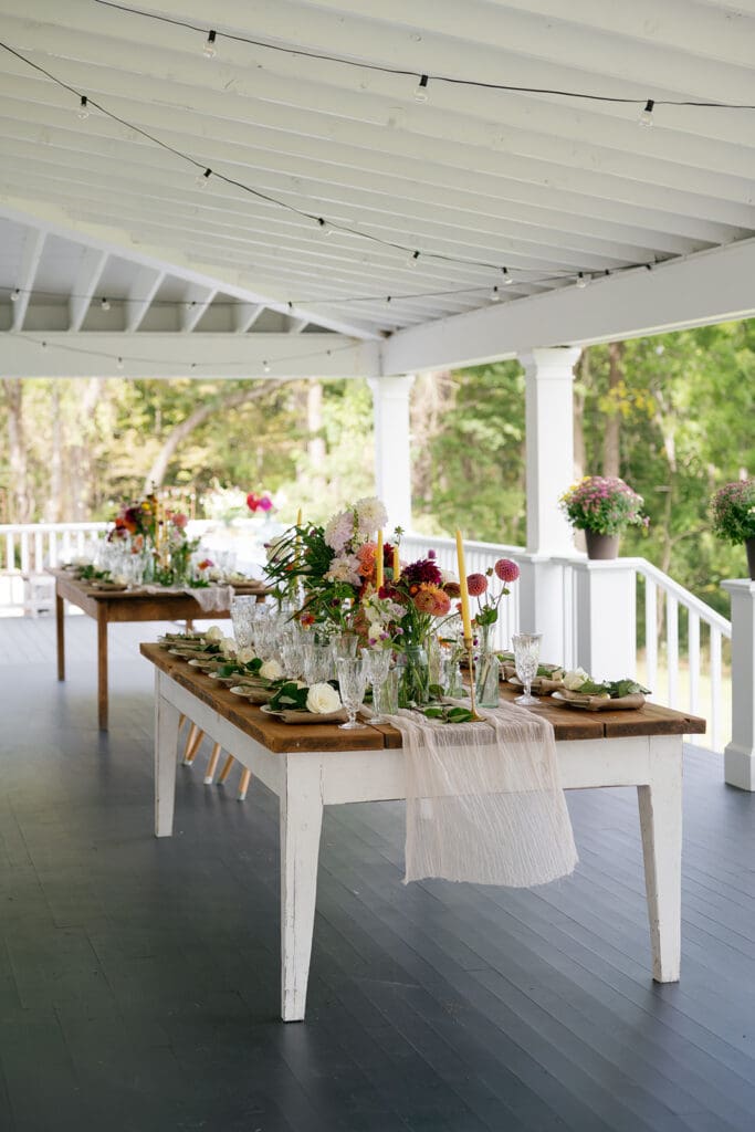 farm house tables on a wraparound porch filled with colorful flowers